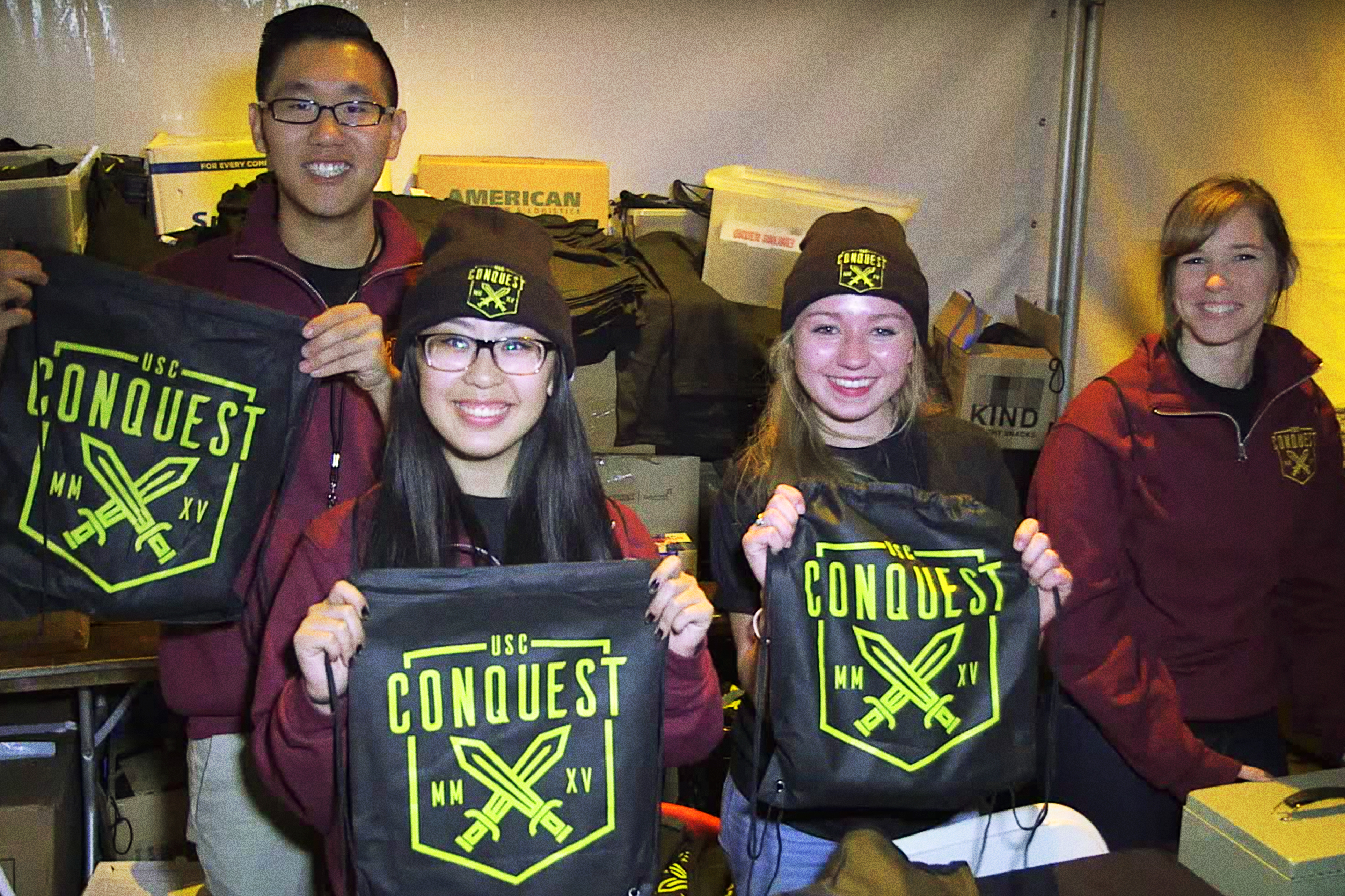 Student government volunteers holding up Conquest merchandise, including bags, hats and beanies